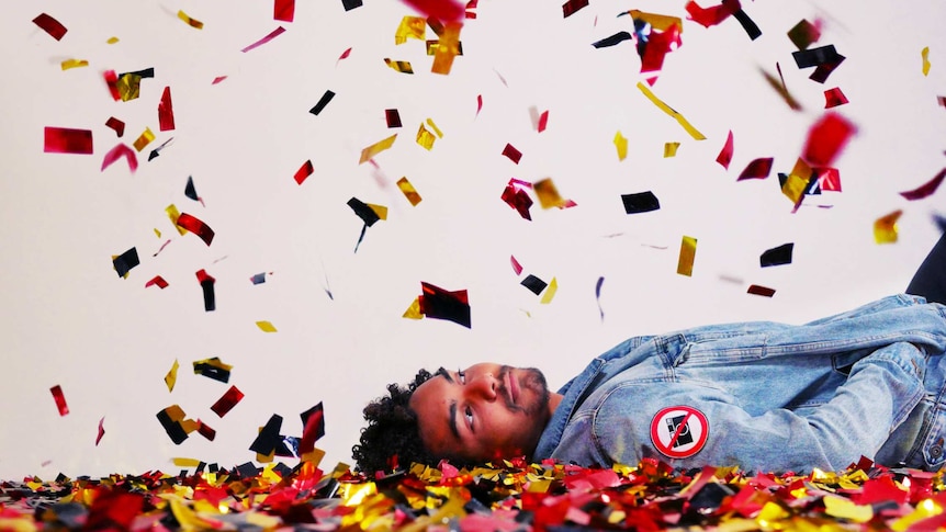 A young man is laying on the ground, looking up at confetti as it rains down on him.