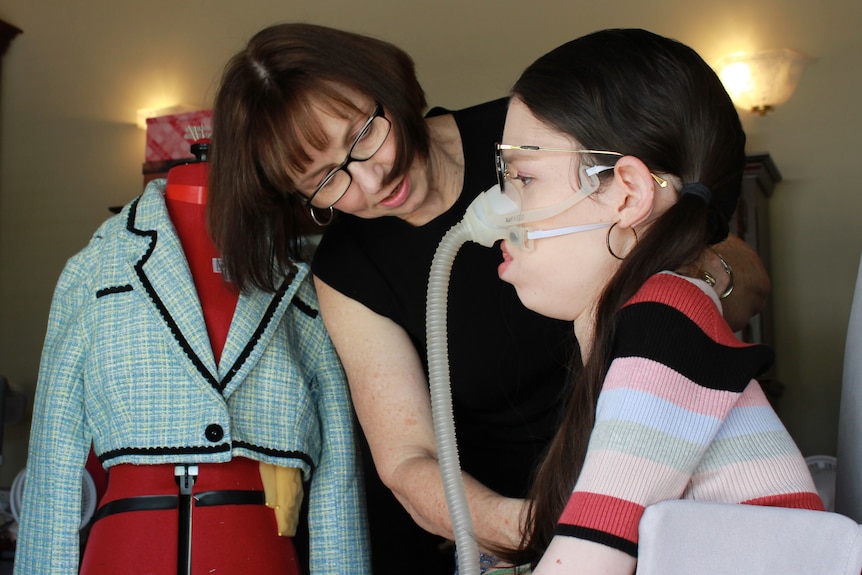 A side-on shot of Catherine Evans working on her daughter Amy's outfit with a mannequin in the background.