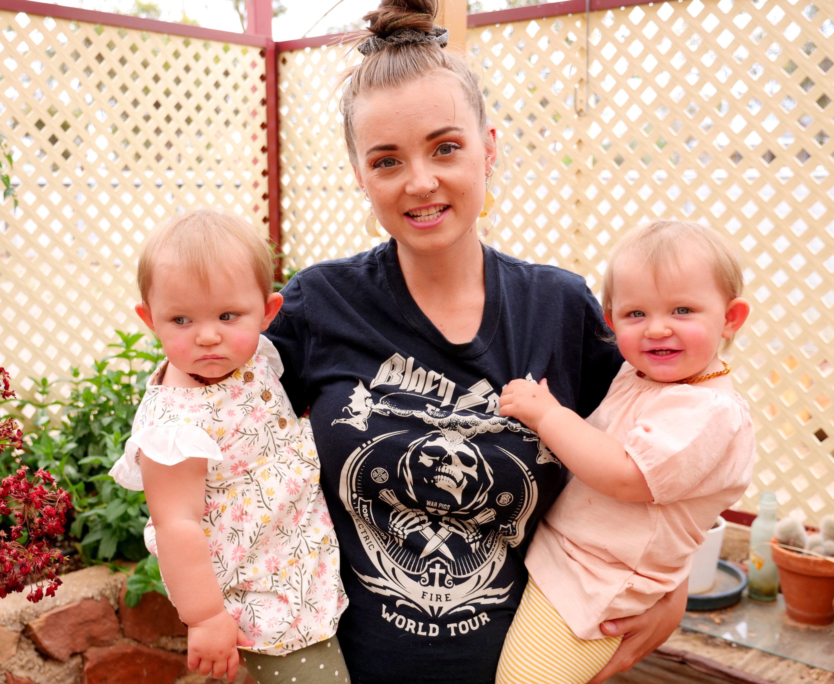 a mum holds her twin girls in both her arms smiling 
