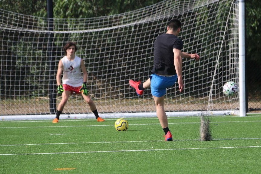 A man kicks a ball at a goalkeeper in practice on Mitchelton Soccer Club's artificial field.