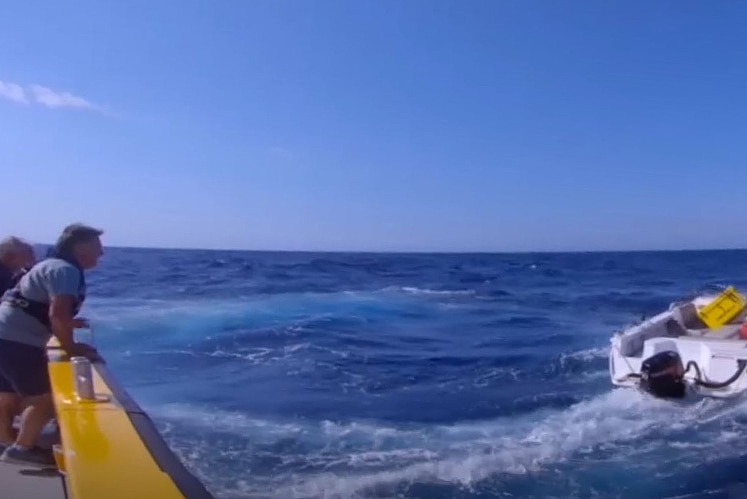 Two men on a big boat looking at a smaller boat nearby in choppy seas.