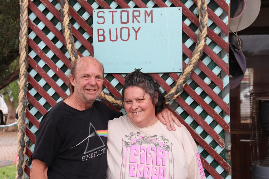 Man with arm around woman both smiling at camera in front of lattice paneling with sign saying Storm Buoy.