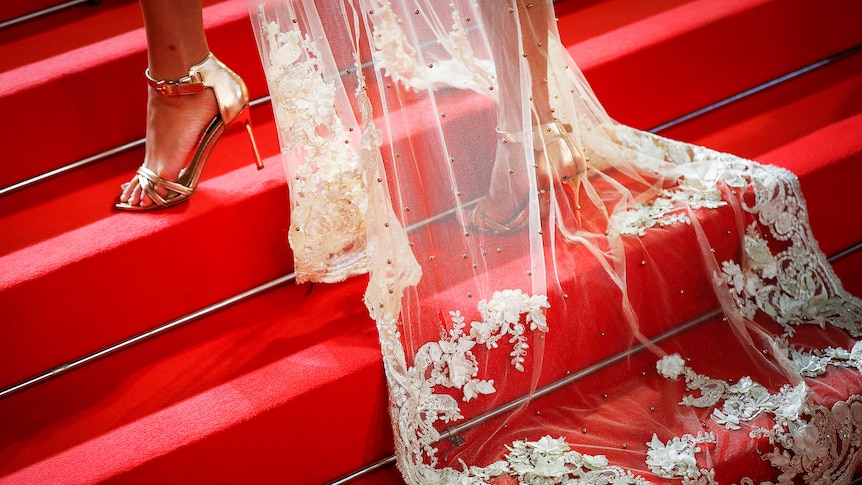 An unidentified woman in gold shoes and a long lace train walking up stairs