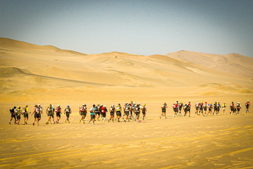 A group of people running through sand dunes under a blue sky=