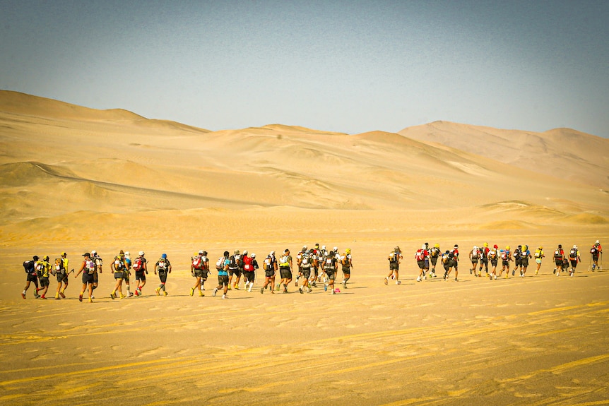 Un groupe de personnes courant à travers les dunes de sable sous un ciel bleu =