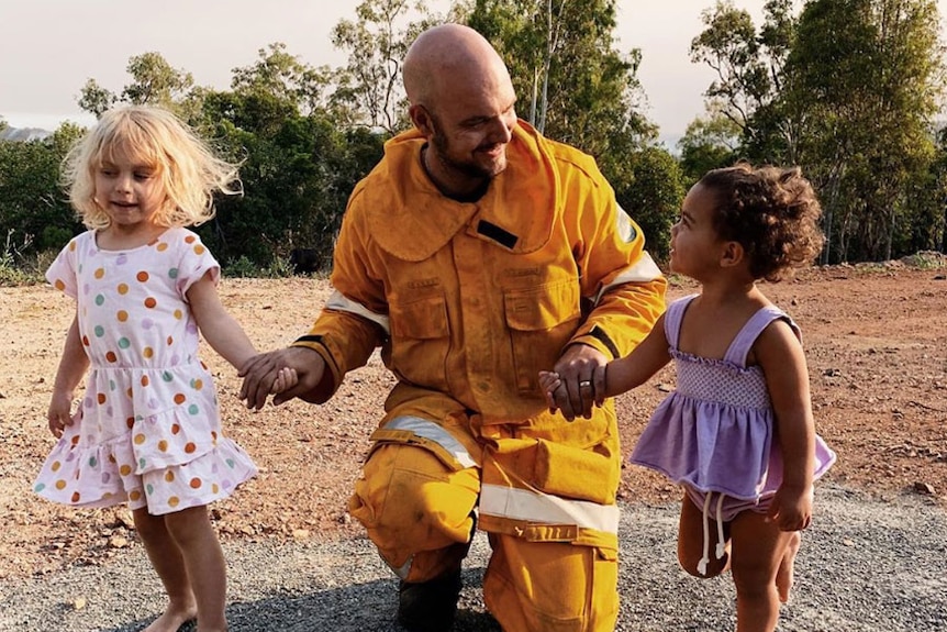 Firefighter Temil Ludwig kneels on the ground as he is greeted by his two children.