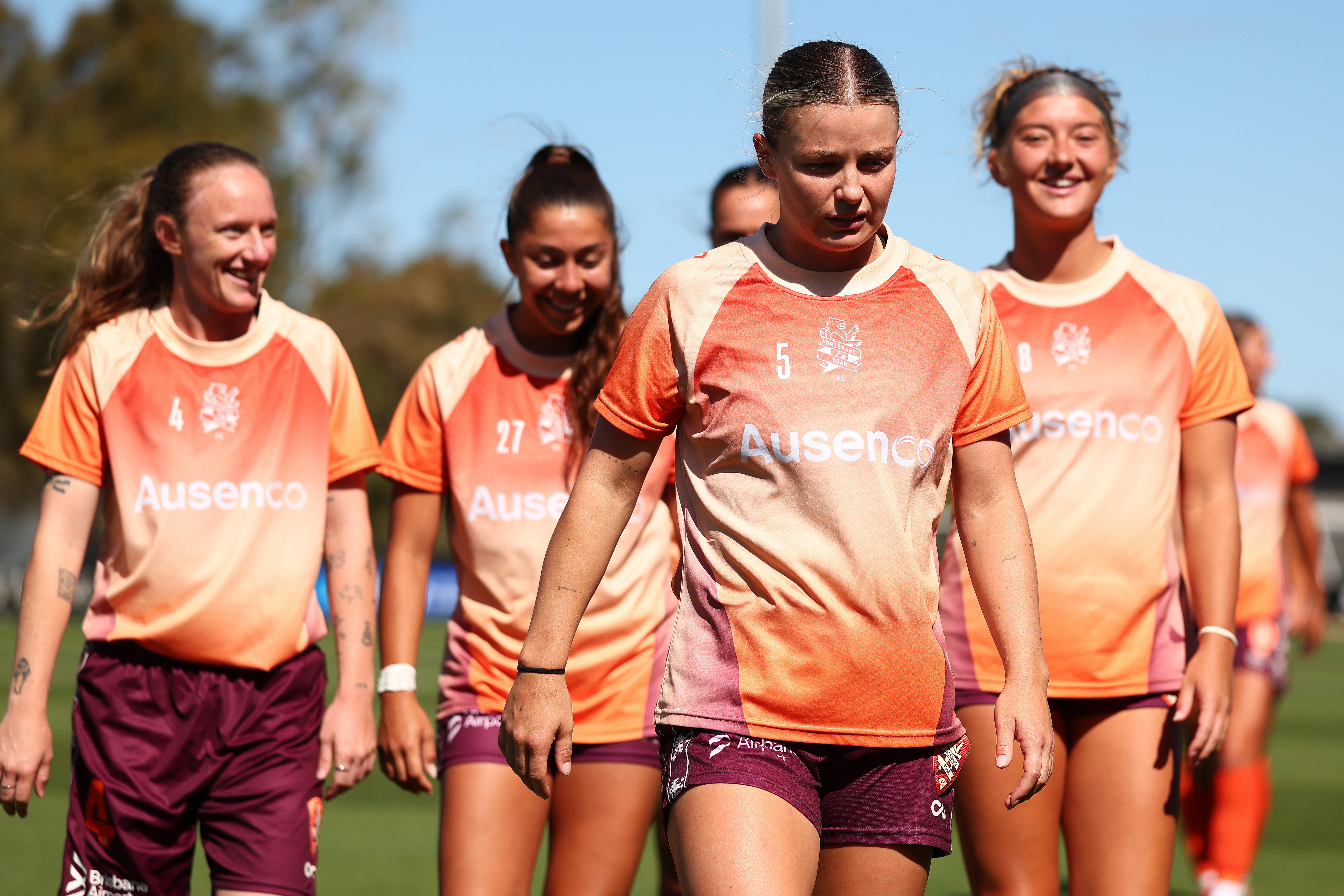 A group of women in orange shirts walk across a football field. 