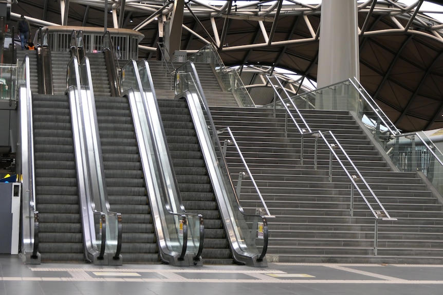 Three empty escalators and two empty staircases in a train station.