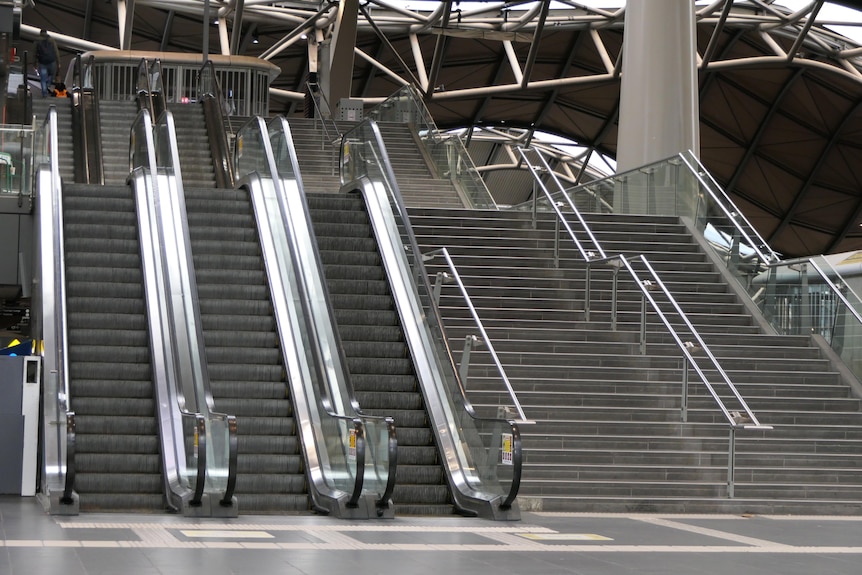 Tres escaleras mecánicas vacías y dos escaleras vacías en una estación de tren.