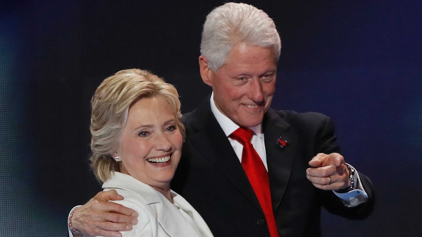 Bill Clinton points while having his arm around Hillary Clinton
