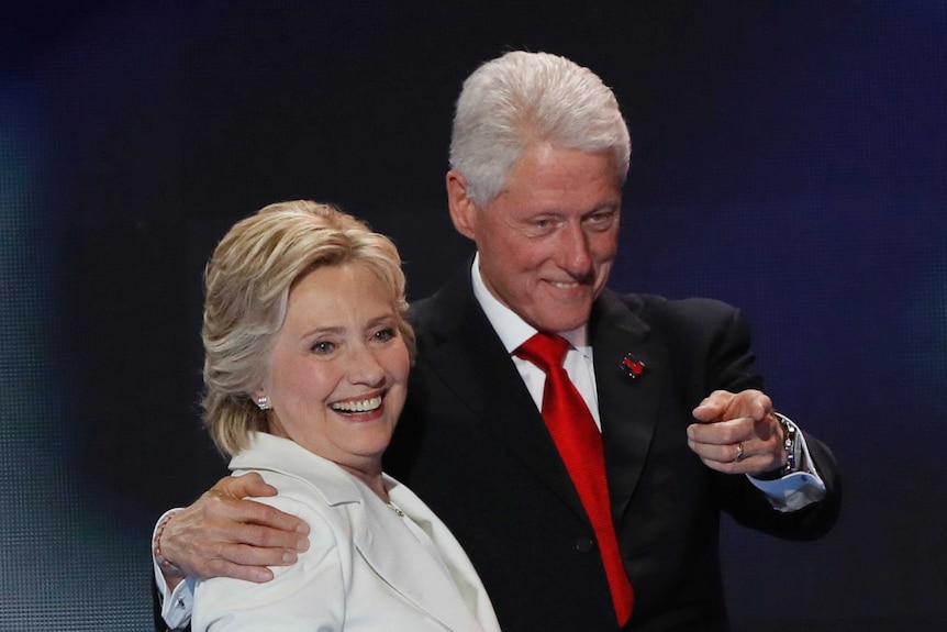 Bill Clinton points while having his arm around Hillary Clinton