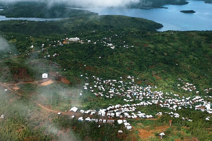 An aerial view shows a small village dotted with white rooftops, near the sea