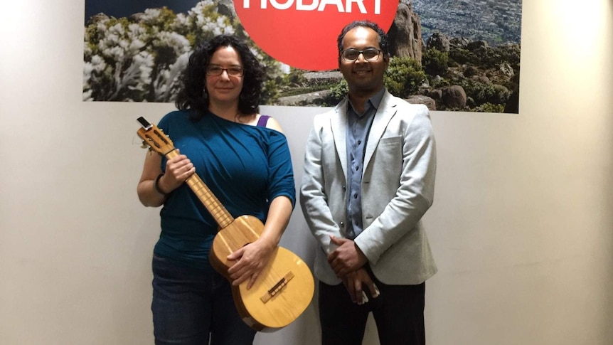 A woman holds a guitar, standing next to a man in a light coloured blazer