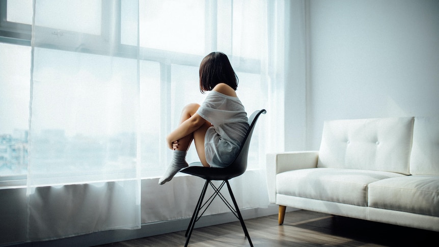 An image of a young person sitting alone in an apartment.