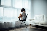 An image of a young person sitting alone in an apartment.