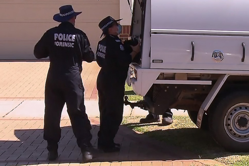 Two police forensic officers standing at the rear of a vehicle in front of a house and driveway.