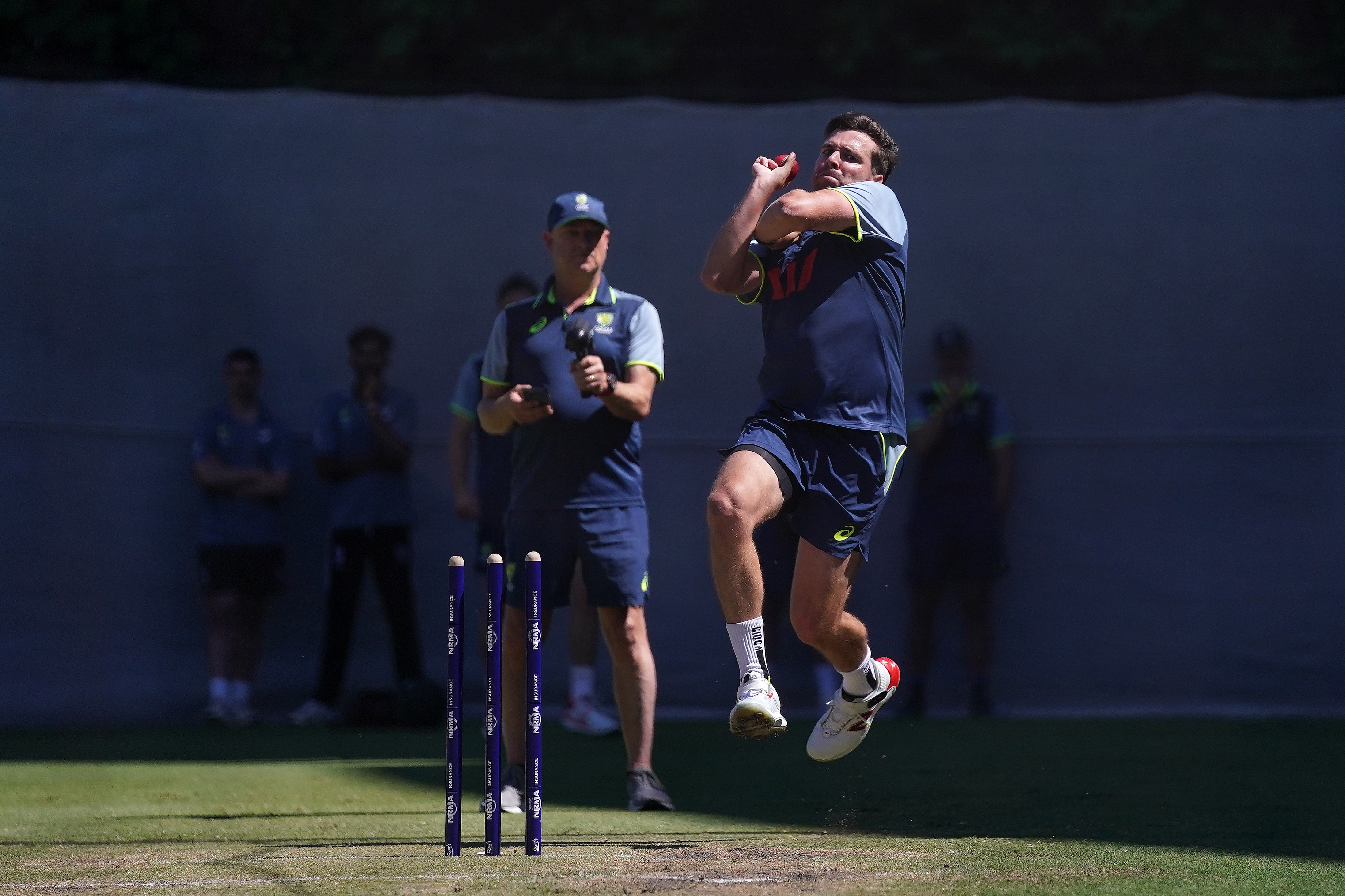 Jhye RIchardson joga boliche em uma sessão de treinamento de críquete australiano enquanto um treinador assiste.
