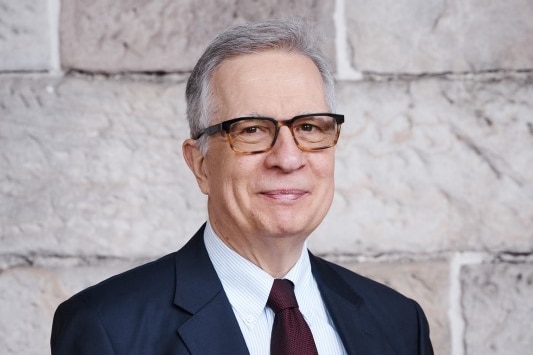 A man wearing glasses and a suit looks at the camera.