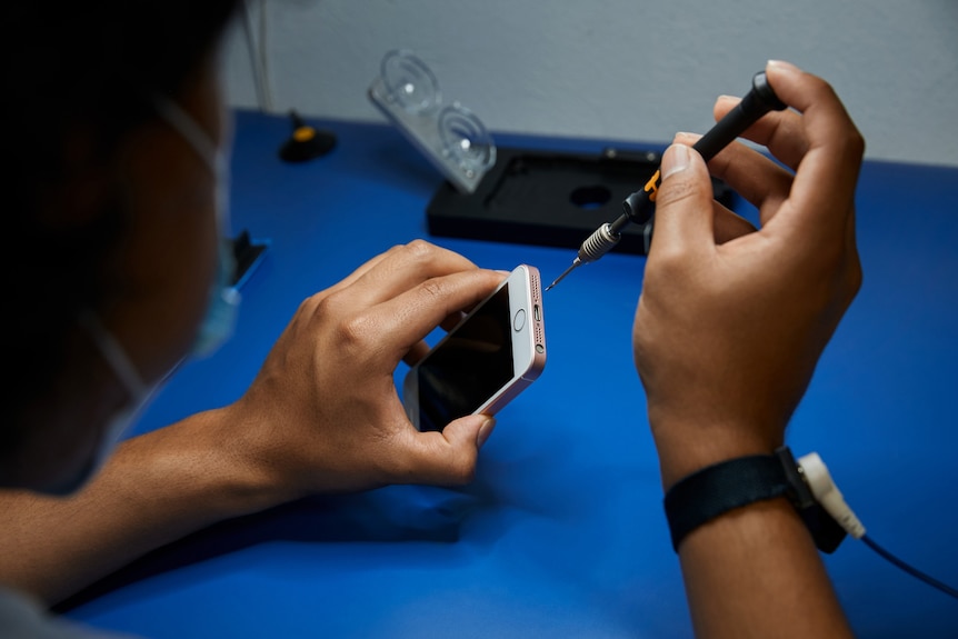 A pair of hands, holding an Apple iPhone and a repair screwdriver