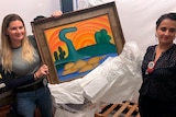 Two women stand either side of Tarsila do Aarel's painting.