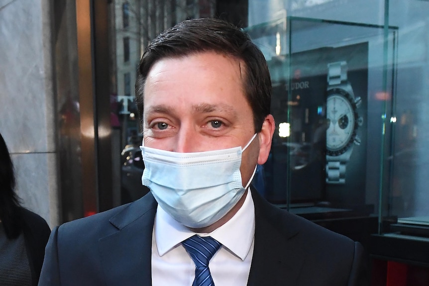 Matthew Guy is flanked by reporters on a CBD street, wearing a face mask.