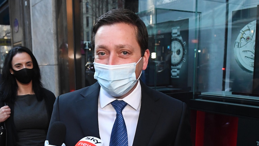 Matthew Guy is flanked by reporters on a CBD street, wearing a face mask.