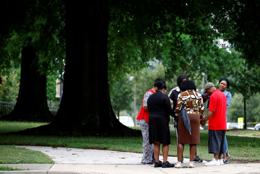 Six people stand in a circle, holding hands with heads bowed in prayer.