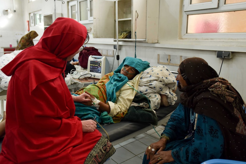 A doctor speaks to a woman lying in a hospital bed.