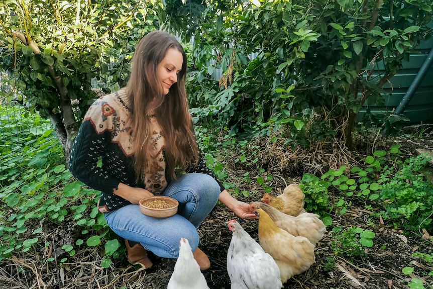 A woman feeds chickens from her hand in her garden.