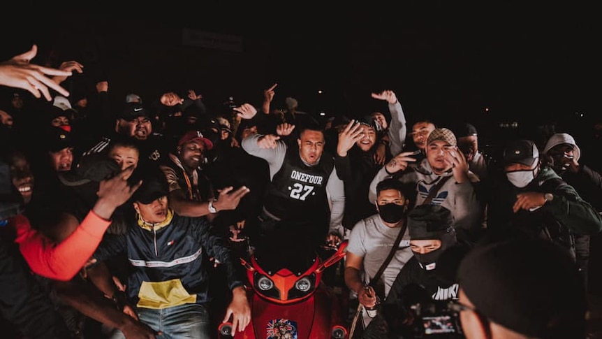 A group of rappers standing in a street at night