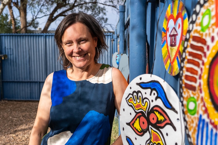 Smiling woman in front of brightly colored aboriginal art