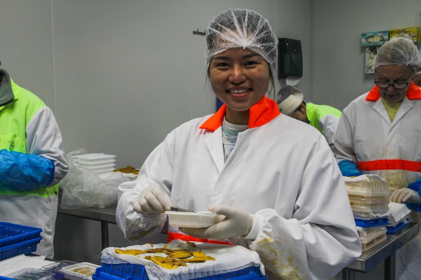 a Malyasian worker smiles at a camera in a sea urhcin factory wearing a hair net.