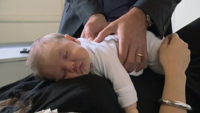 Baby lying at mother's chest receiving chiropractor treatment.