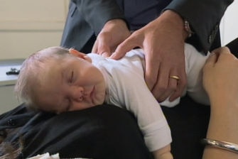 Baby lying at mother's chest receiving chiropractor treatment.
