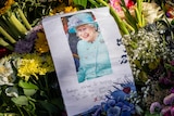 Numerous bouqets of flowers lay on the ground, beneath a photo and note to Queen Elizabeth II