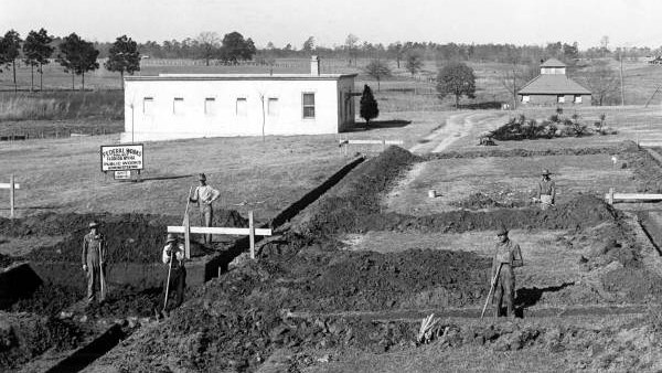 A black and white image of a construction site with a small white shack in the background.