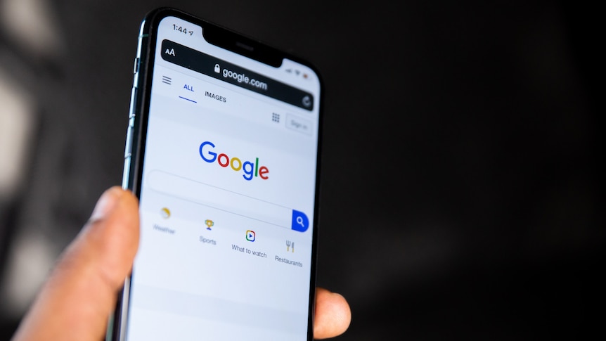 A close up of a hand holding an Apple iPhone, which displays the Google homepage