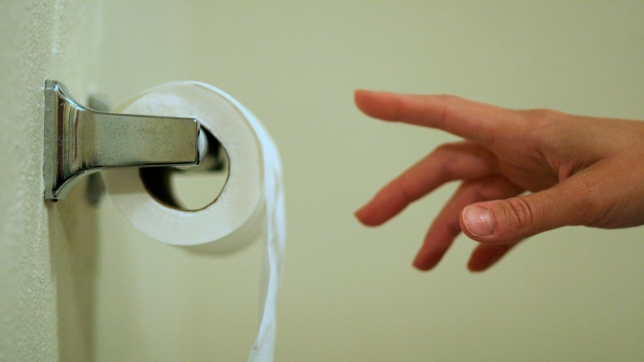 A hand reaching for a sheet of toilet paper