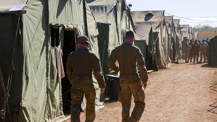 Soldiers walk past a row of large tents