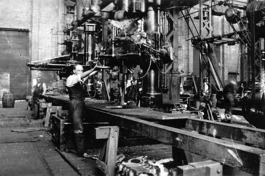 A black and white photograph of a worker in an industrial setting inside the old Midland Railway Workshops.
