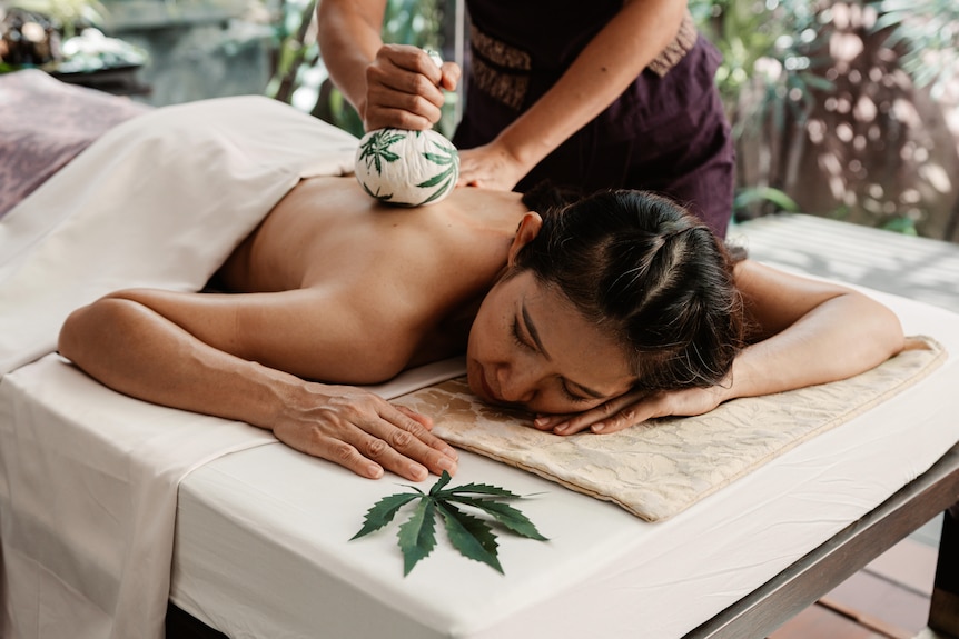 A woman getting a massage with a massage cloth with a marijuana leaf on it. 
