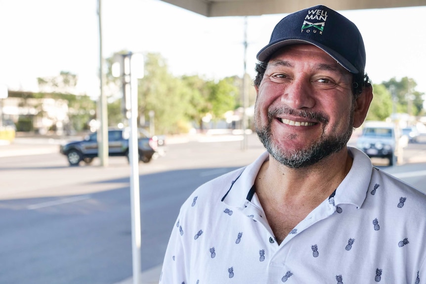 A man with a greying beard wearing a cap smiles at the camera.