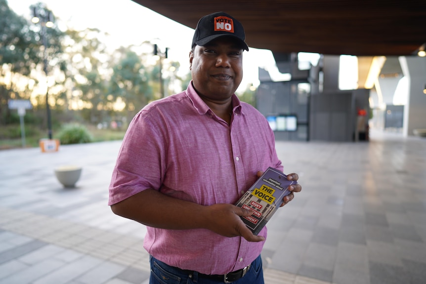 A man in a pink shirt and a No hat holding The Voice brochure