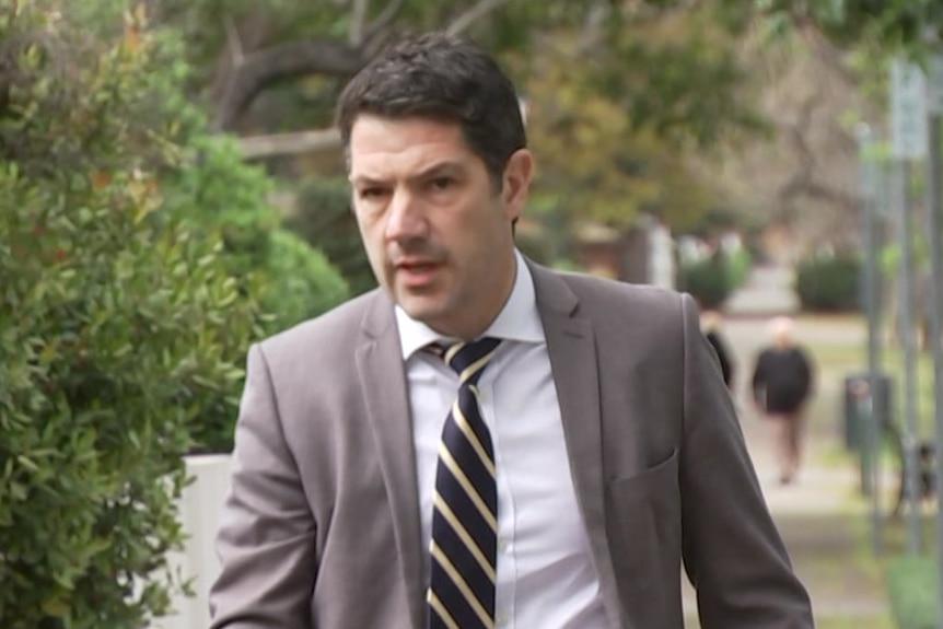 A man wearing a grey suit and tie walking