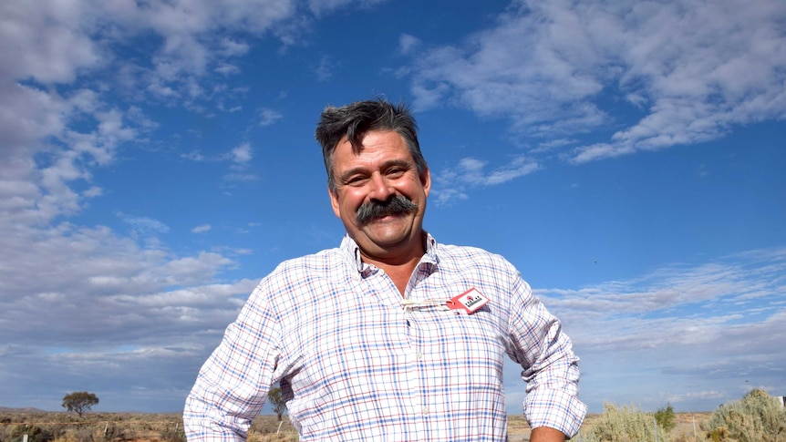 A man with a moustache smiles at the camera in rural SA.