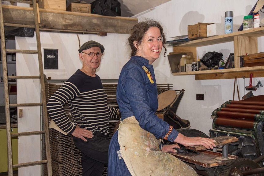 A man and a woman work at vintage presses in an artist's studio