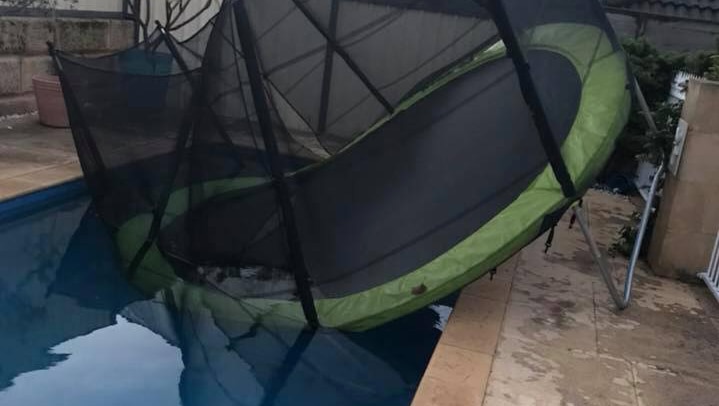 A trampoline partially submerged in a backyard swimming pool.