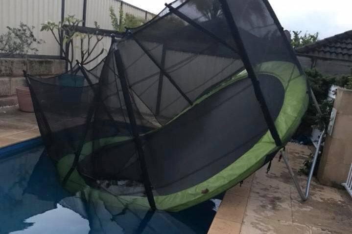 A trampoline partially submerged in a backyard swimming pool.