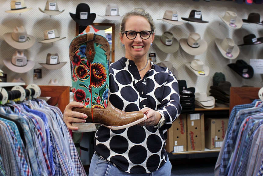 Hannah Hacon standing in her western wear shop, holding a cowboy boot