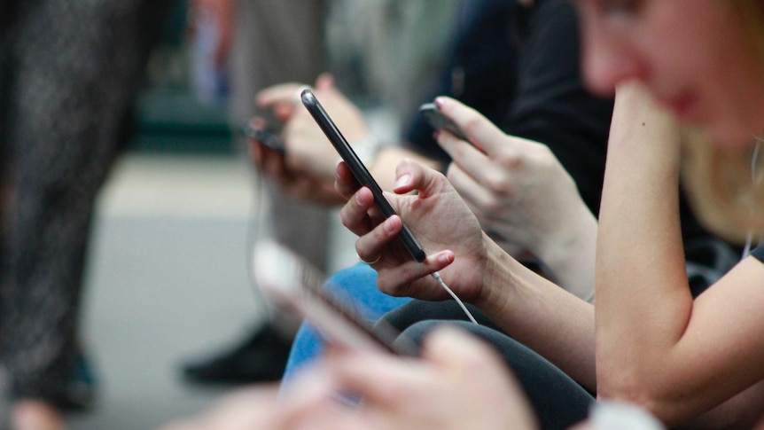 People sitting on a bench looking at their mobile phones